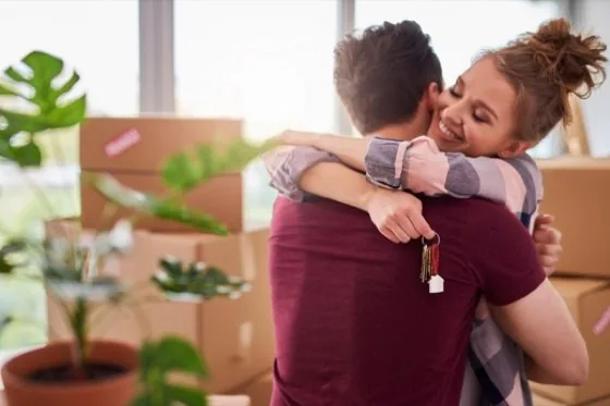 A couple hugging among moving boxes, holding the keys to their new home
