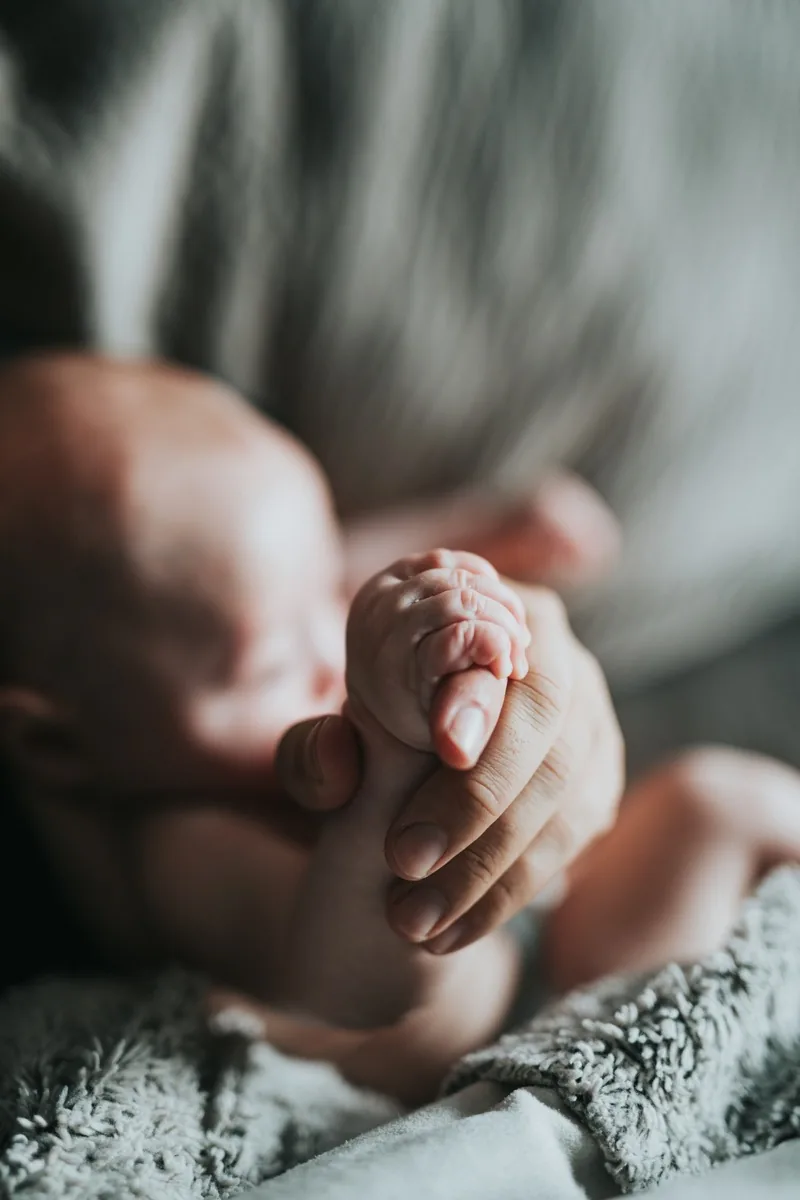 A newborn baby&rsquo;s hand gripping an adult&rsquo;s finger